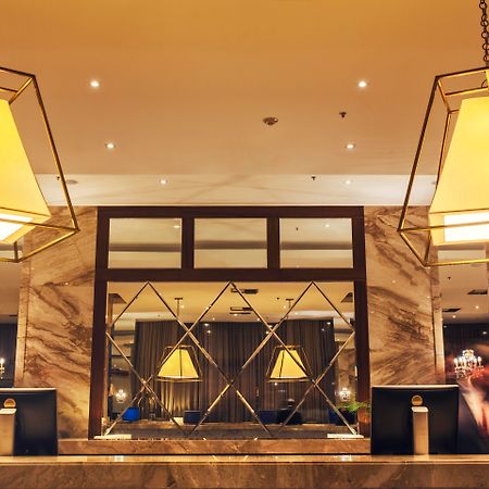 Windsor Marapendi Hotel Rio de Janeiro Eksteriør billede The photo shows a hotel lobby or reception area. There are large geometric light fixtures hanging from the ceiling, providing a warm glow to the space. The reception desk is made of a polished material, likely marble, with decorative elements and two