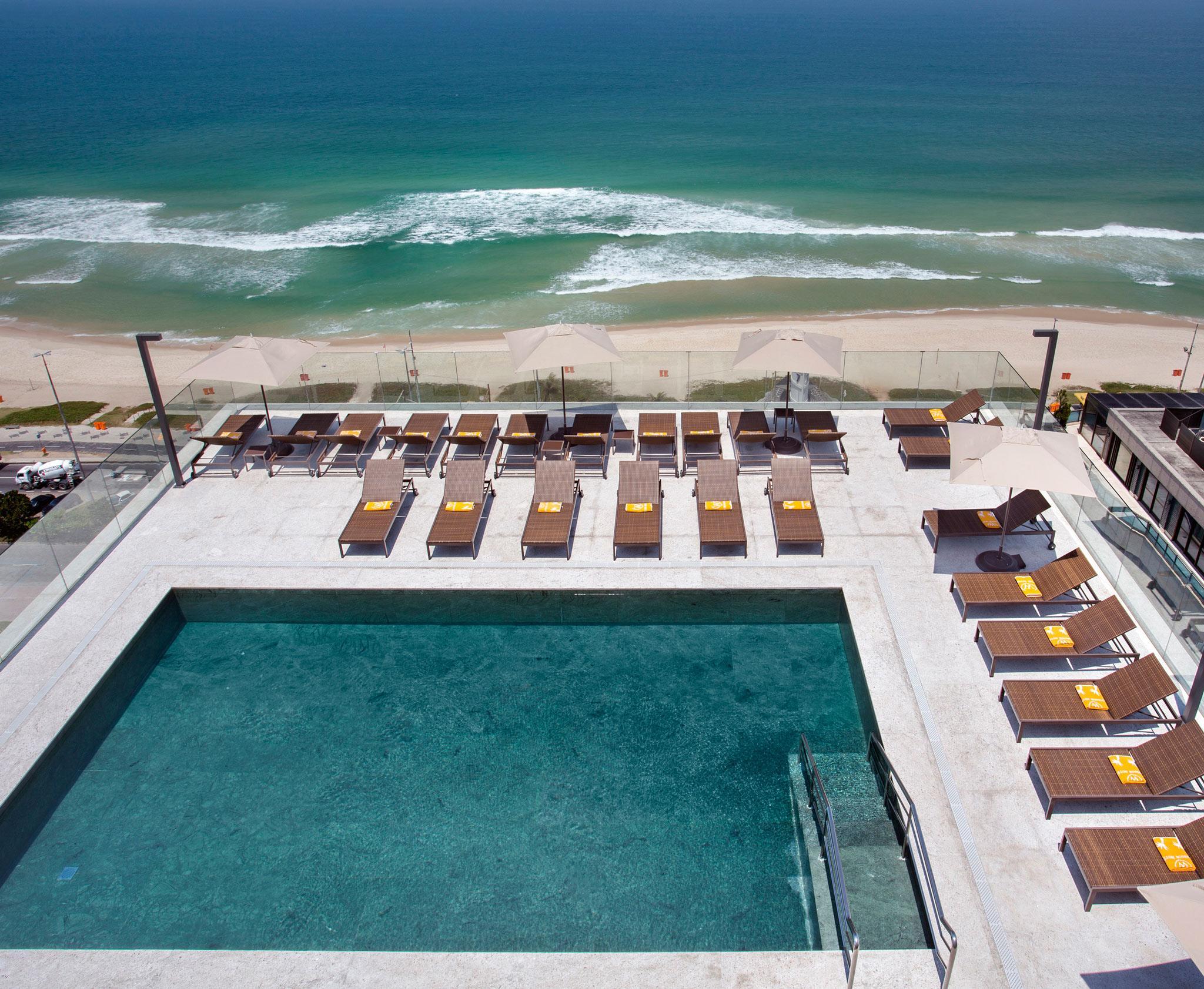 Windsor Marapendi Hotel Rio de Janeiro Eksteriør billede The photo shows a rooftop area with a swimming pool and several lounge chairs arranged around it. The pool has a clear blue surface, and the lounge chairs are positioned in a neat row, some with yellow cushions. In the background, you can see a beaut