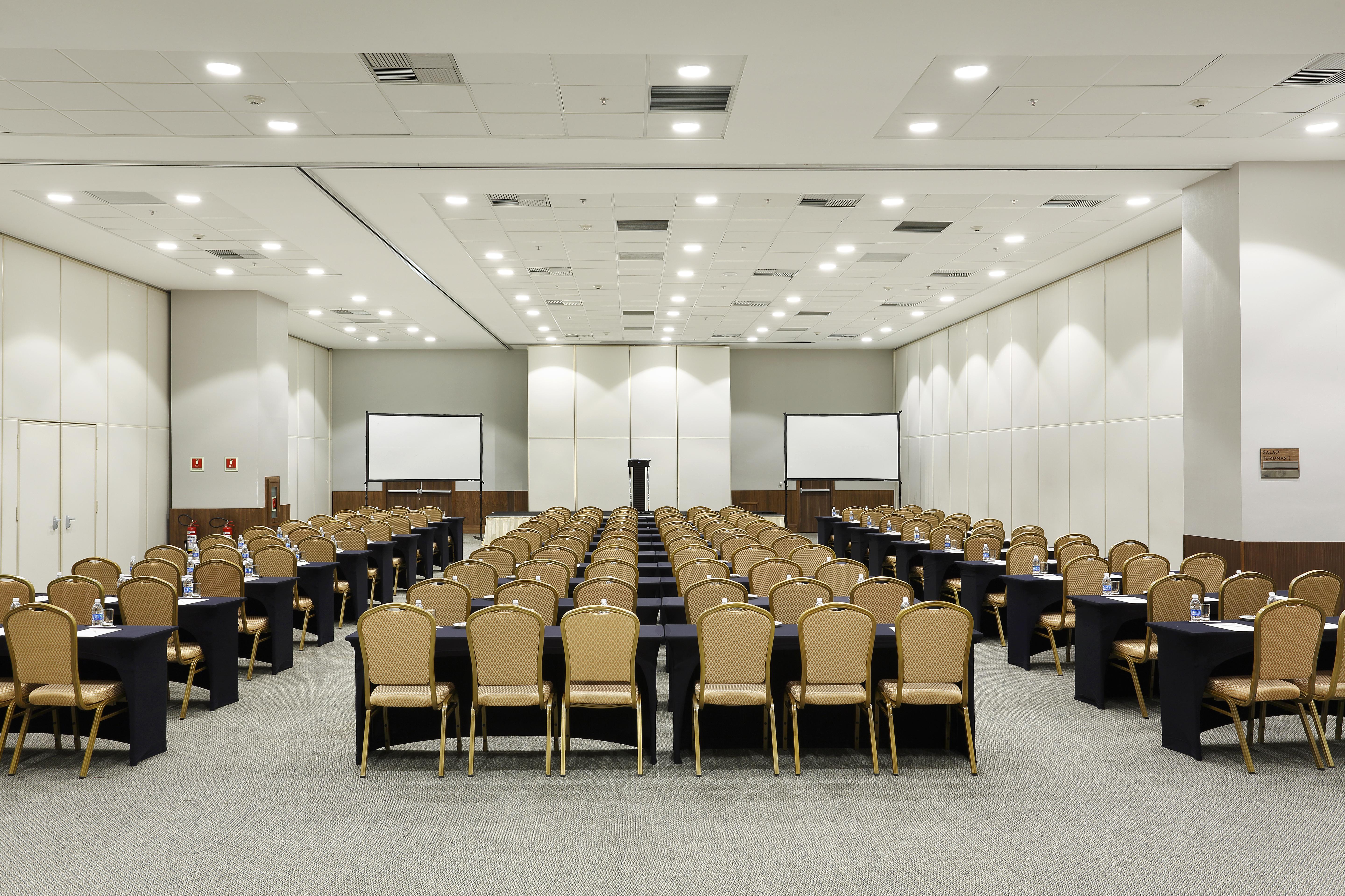 Windsor Marapendi Hotel Rio de Janeiro Eksteriør billede The photo shows a conference room arranged for an event or meeting. There are rows of neatly arranged chairs with golden frames, paired with black tables. The room has bright overhead lighting and features two blank screens in the front, likely for p