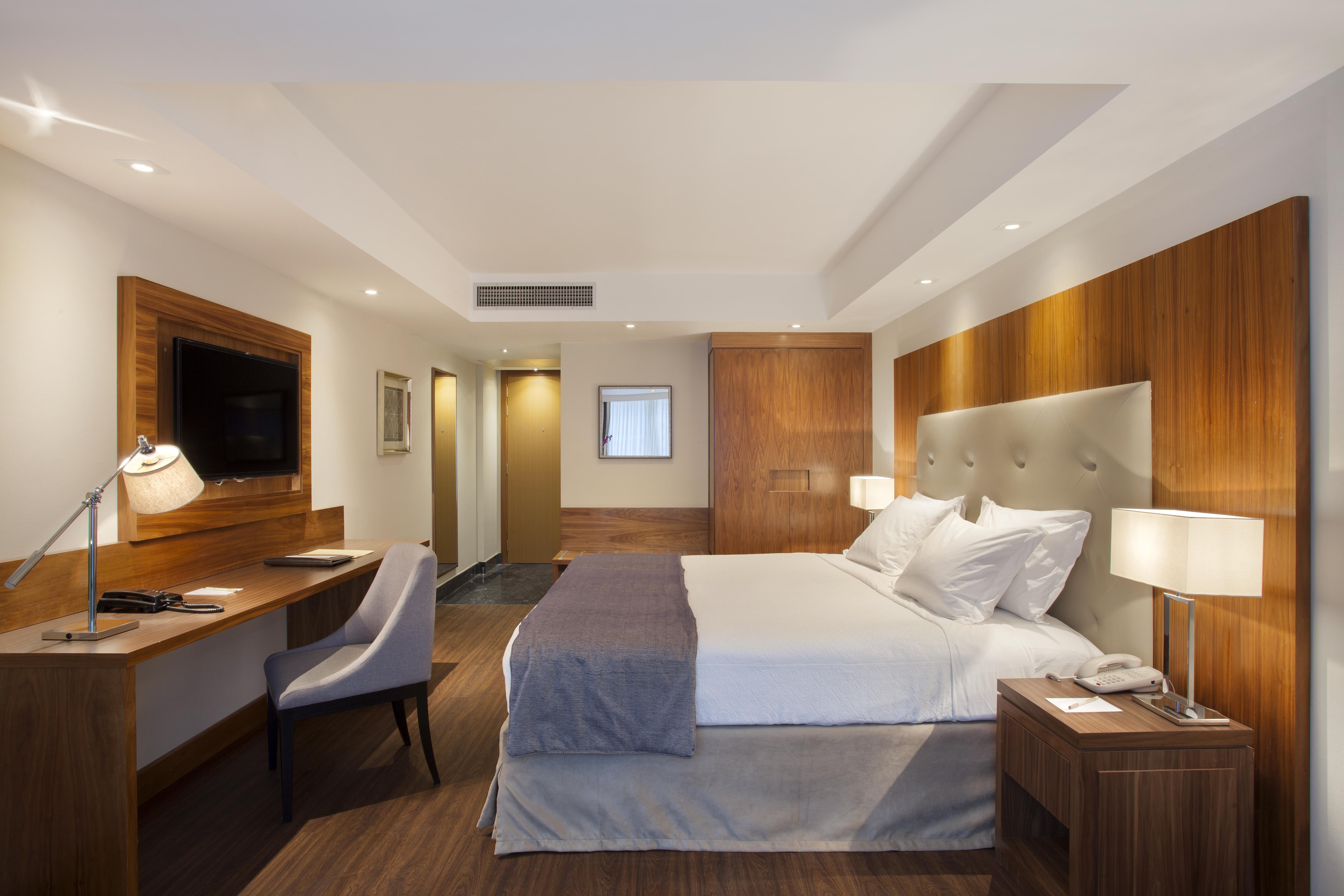Windsor Marapendi Hotel Rio de Janeiro Eksteriør billede The photo shows a modern hotel room featuring a large bed with white and gray bedding. The headboard is upholstered in light fabric. There are two bedside lamps on either side of the bed, providing warm lighting. A television is mounted on the wall o