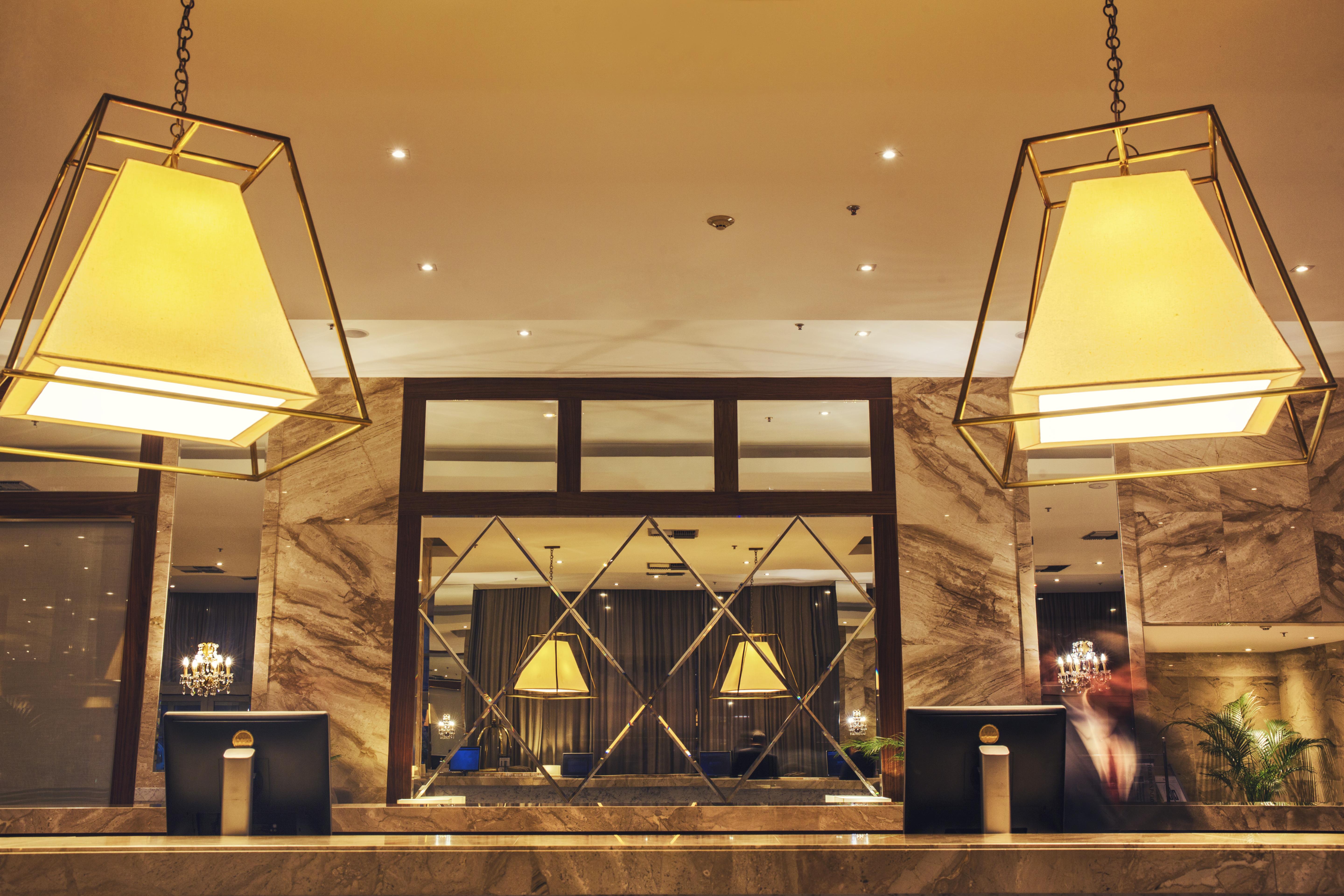 Windsor Marapendi Hotel Rio de Janeiro Eksteriør billede The photo shows a hotel lobby or reception area. There are large geometric light fixtures hanging from the ceiling, providing a warm glow to the space. The reception desk is made of a polished material, likely marble, with decorative elements and two
